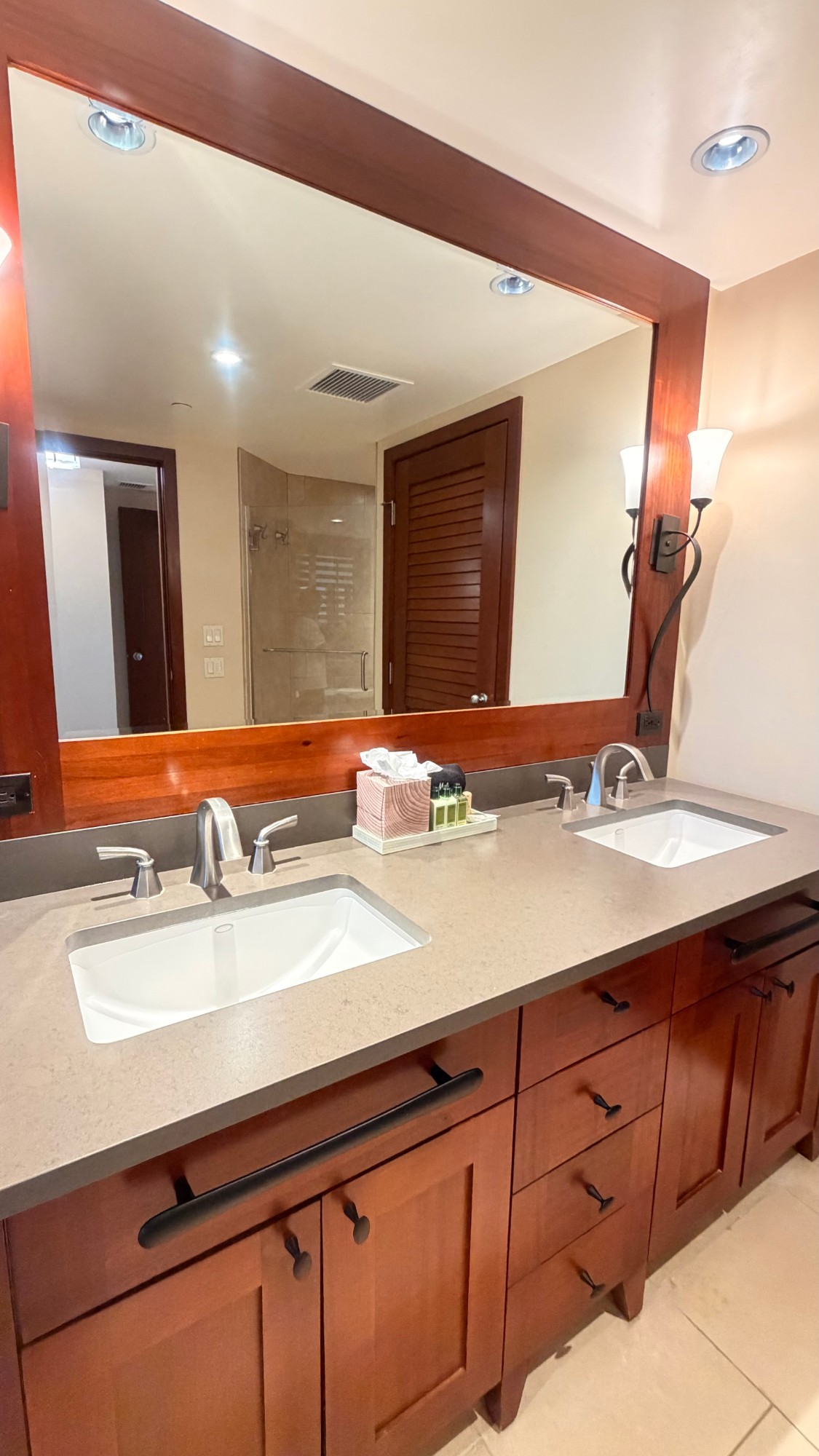 Polished double vanity with wood cabinets, clean sinks and restocked guest toiletries in an Oahu vacation rental bathroom