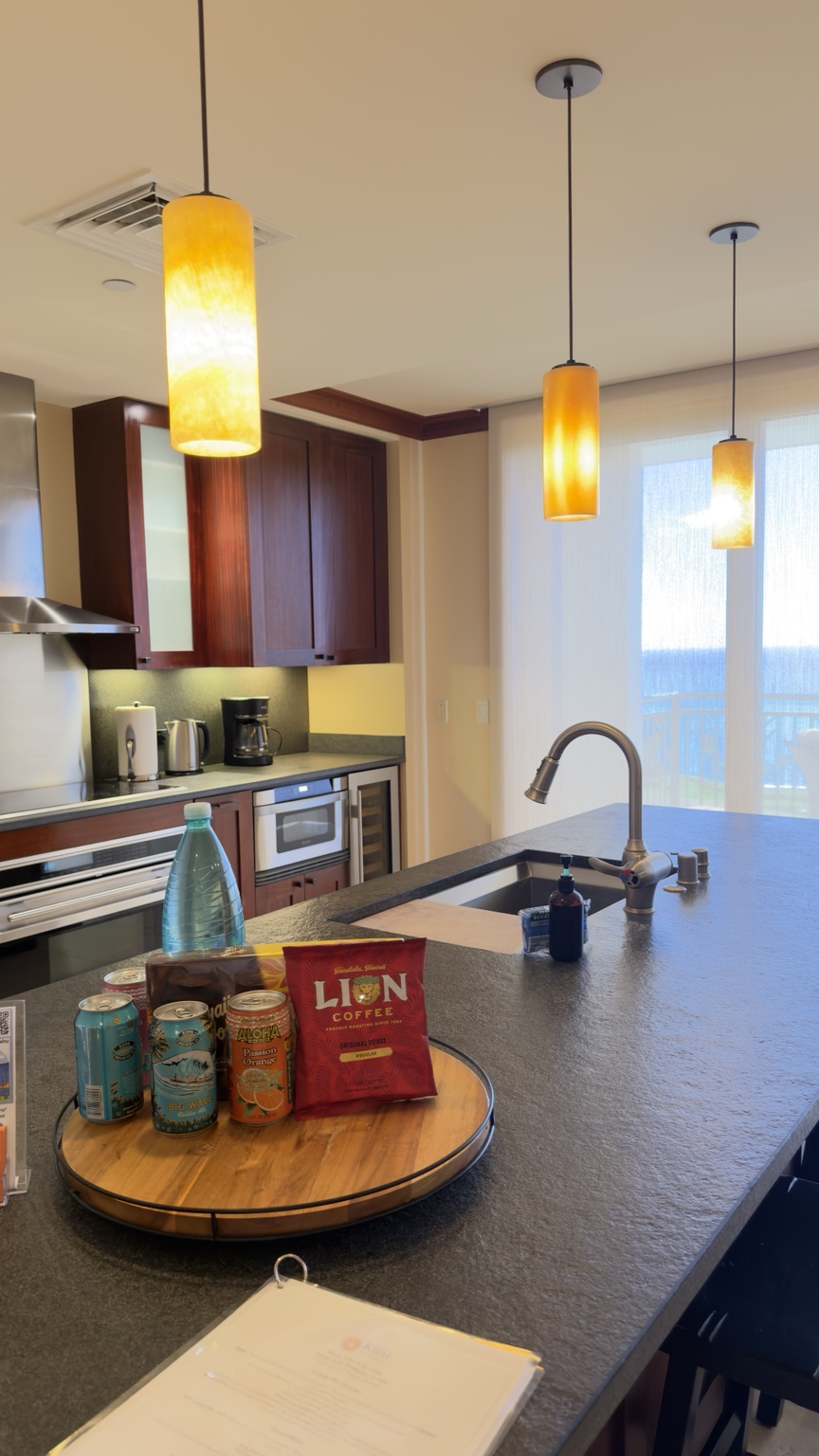 Ko Olina resort kitchen with a welcome tray of local coffee and drinks on a clean granite island, ocean view beyond