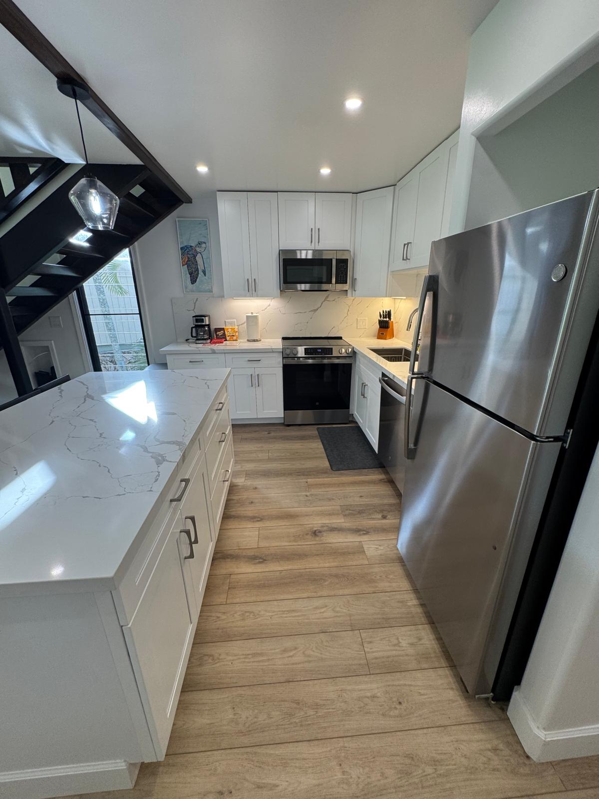 Bright white kitchen with a marble-look island, stainless steel appliances and spotless wood-look floors after a turnover