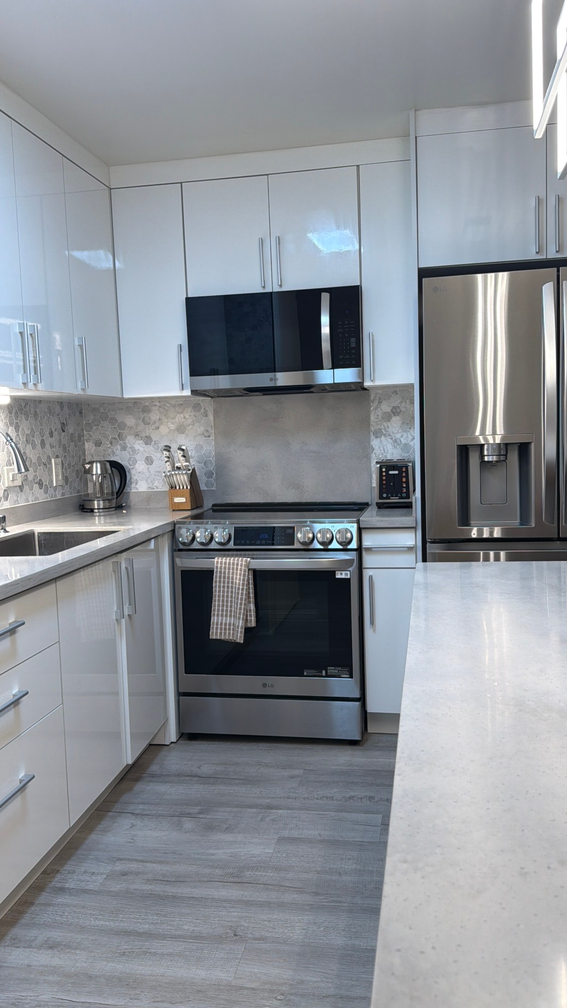 Glossy white kitchen with hexagon tile backsplash, stainless steel LG appliances and a spotless quartz island after a turnover
